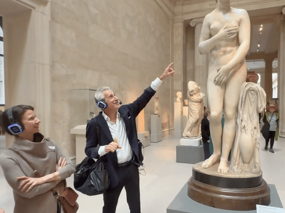 Gene Seidman, wearing a headset, points up at a marble statue while guiding a visitor through a gallery at The Metropolitan Museum of Art